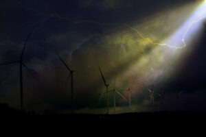 Dark stormy wind turbine field with ray of light.